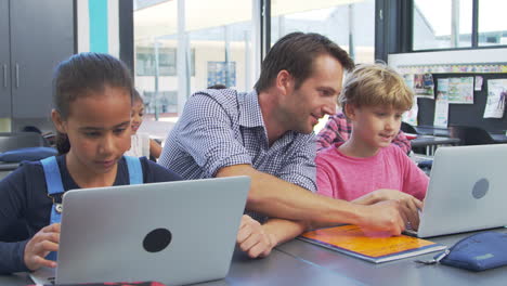 Teacher-helping-young-students-using-laptops-in-class