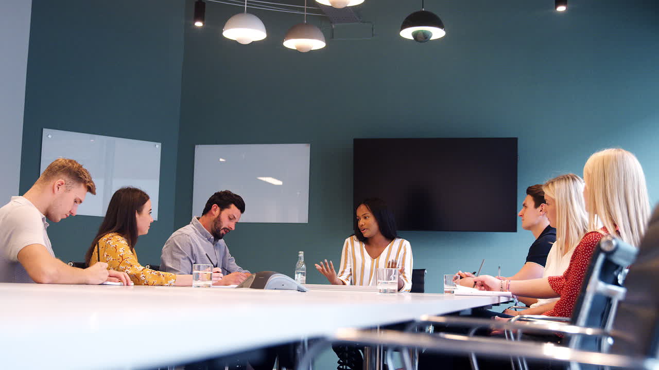 grupo de candidatos reunidos en torno a la mesa de la sala de juntas en el día de evaluación de la contratación de graduados