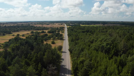 Forwards-fly-above-landscape.-Aerial-panoramic-footage-of-flat-countryside-with-forest.-Tilt-down-on-car-driving-on-road.-Denmark