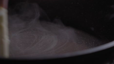 a close up shot of a chef using a block of butter to grease a non stick frying pan, the hot surface melting the butter leaving behind a well coated pan for easy cooking