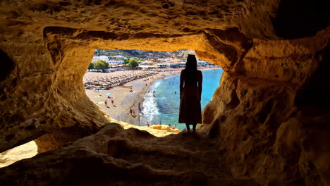 woman gazes out at beaches of rethymno, greece from a cave in venetian fortezza castle