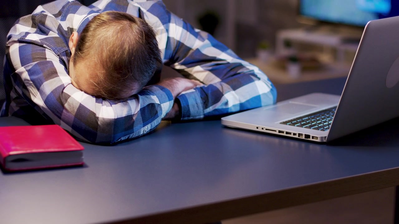 Utmattet mann som sover på skrivebordet på kontoret om natten