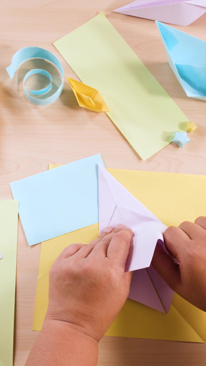 Vista dall'alto di mani che piegano con cura carta viola in un origami indovino.