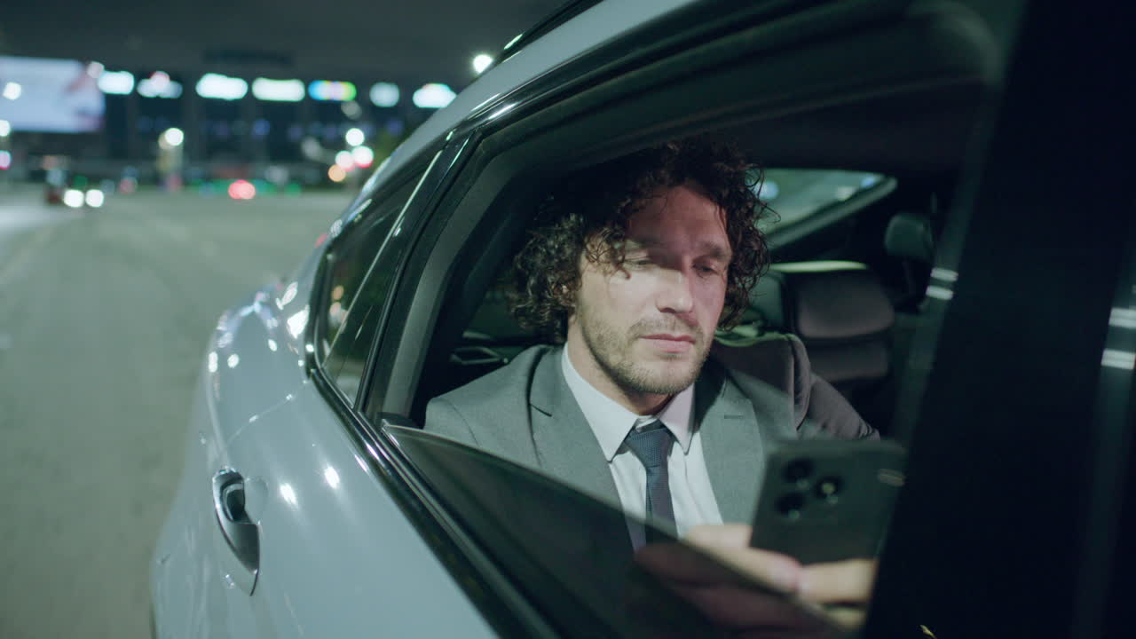 Businessman Texting on Phone and Looking through Car Window at Night