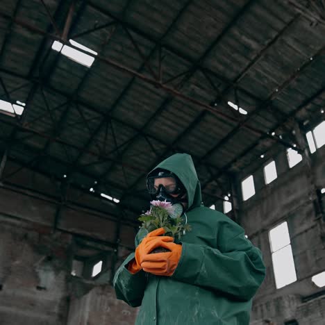 ecologist with plants in abandoned place. person in protective uniform and gas mask holding flowers inside the destroyed building. chemical attack and air pollution