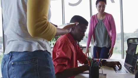 three happy diverse creative male and female colleagues using laptop and tablet talking in office