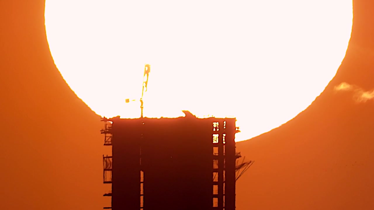 Silhouette of Unfinished Skyscraper Against Large Setting Sun