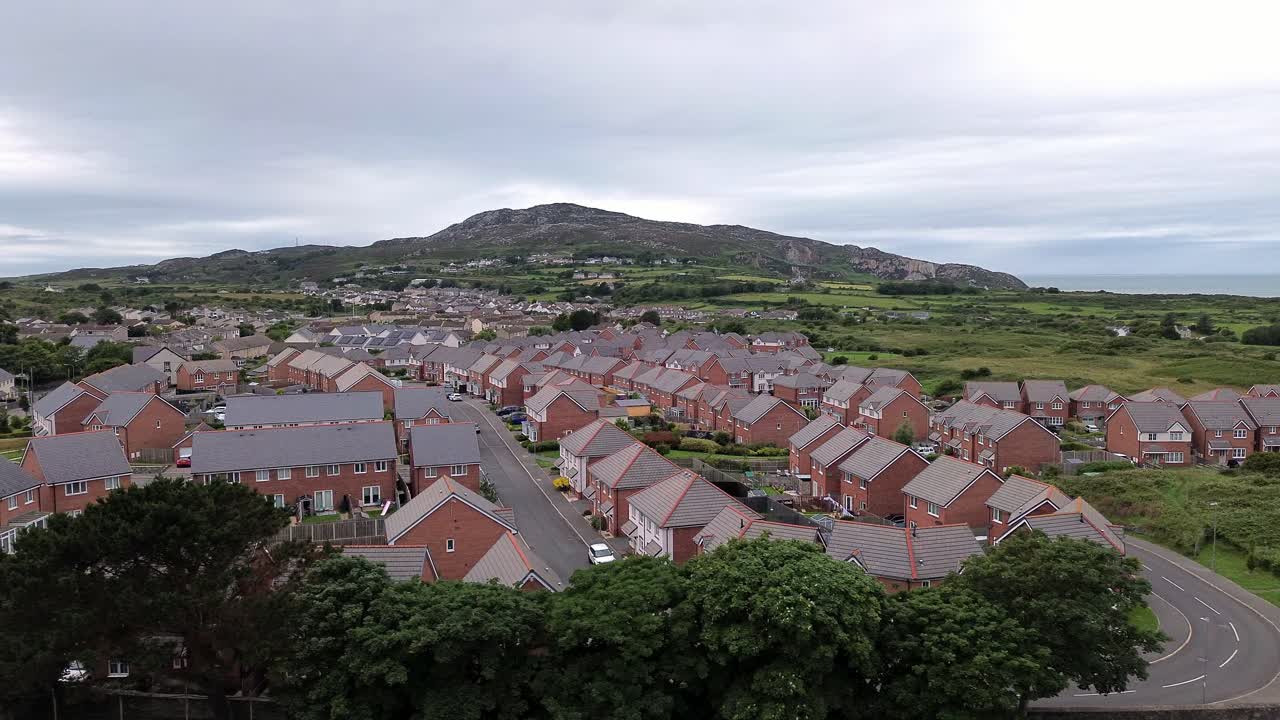 Aerial view orbit across modern red brick housing neighbourhood under Holyhead mountain in Wales