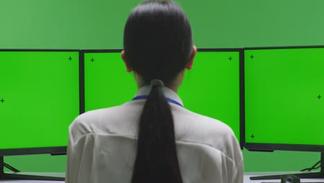 person facing away from a computer with green screens