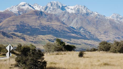 Panoramaaufnahme-Einer-Einsamen-Straße-Und-Einer-Massiven-Schneebedeckten-Bergkette-Im-Hintergrund---Gletscherbrandspur,-Neuseeland