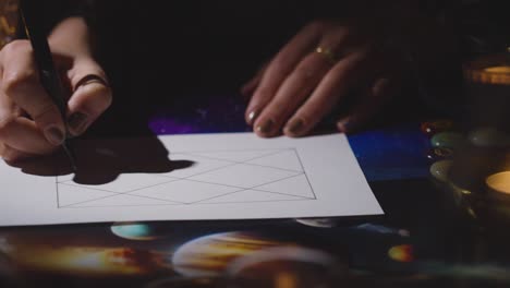 primer plano de una mujer dibujando astrología lagna o gráfico de nacimiento en la mesa a la luz de las velas 5
