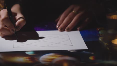 close up of woman drawing astrology lagna or birth chart on candlelit table 5