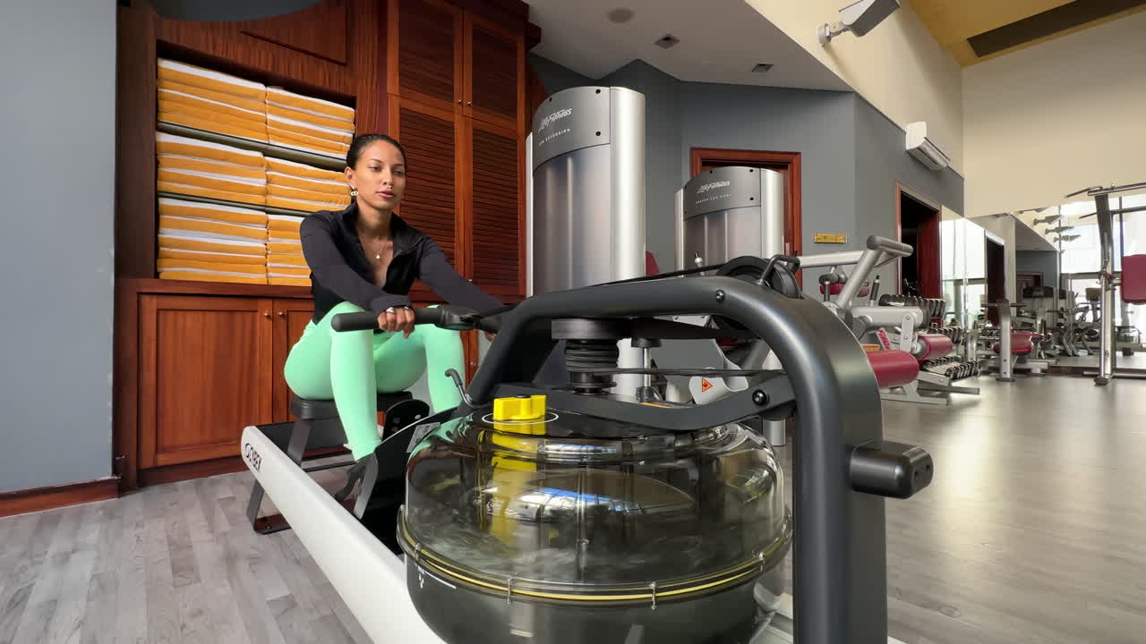 disparo en cámara lenta de una atleta femenina usando una máquina de resistencia de remo dentro de un gimnasio
