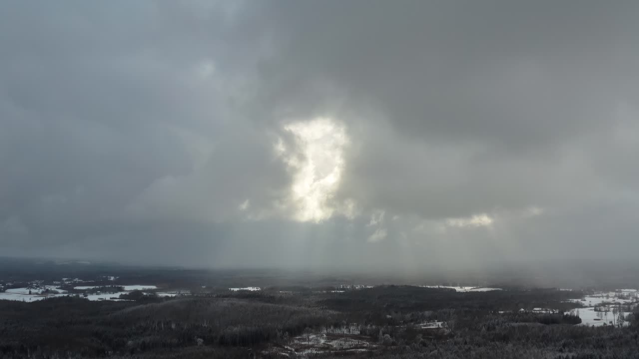 Sun rays breaking through thick clouds in winter. Aerial view over the countryside landscape. Snow storm approaching.