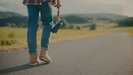 Man-Holding-Camera-While-Walking-On-Road