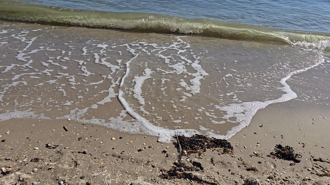 Havbrænding på sandstranden: Blide bølger bryder på fladt, lyst sand