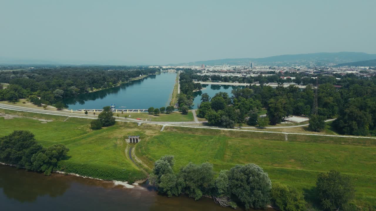 broad grassy riverbank leads to Lake Jarun with Zagreb stretching under hazy summer air