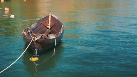 a fishing boat is moored at the shore slowly swinging on a wave in a clear summer day 4k video