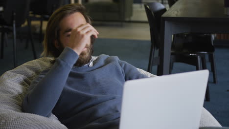 caucasian businessman sitting on pouf using a laptop in modern office