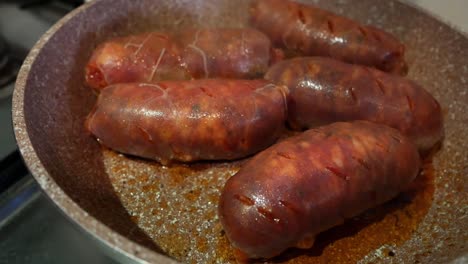 very close up of some big and bright red chorizo sausages being cooked on a pan