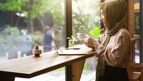 an upwardly mobile asian muslim woman enjoying a relaxing moment in the coffee shop on a bright sunny day