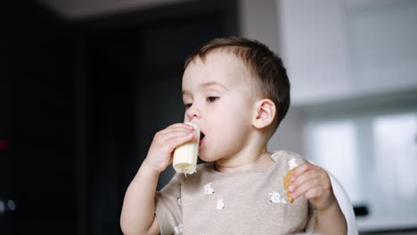 little kid is eating holding food in both hands. lovely baby boy eating banana. low angle view.