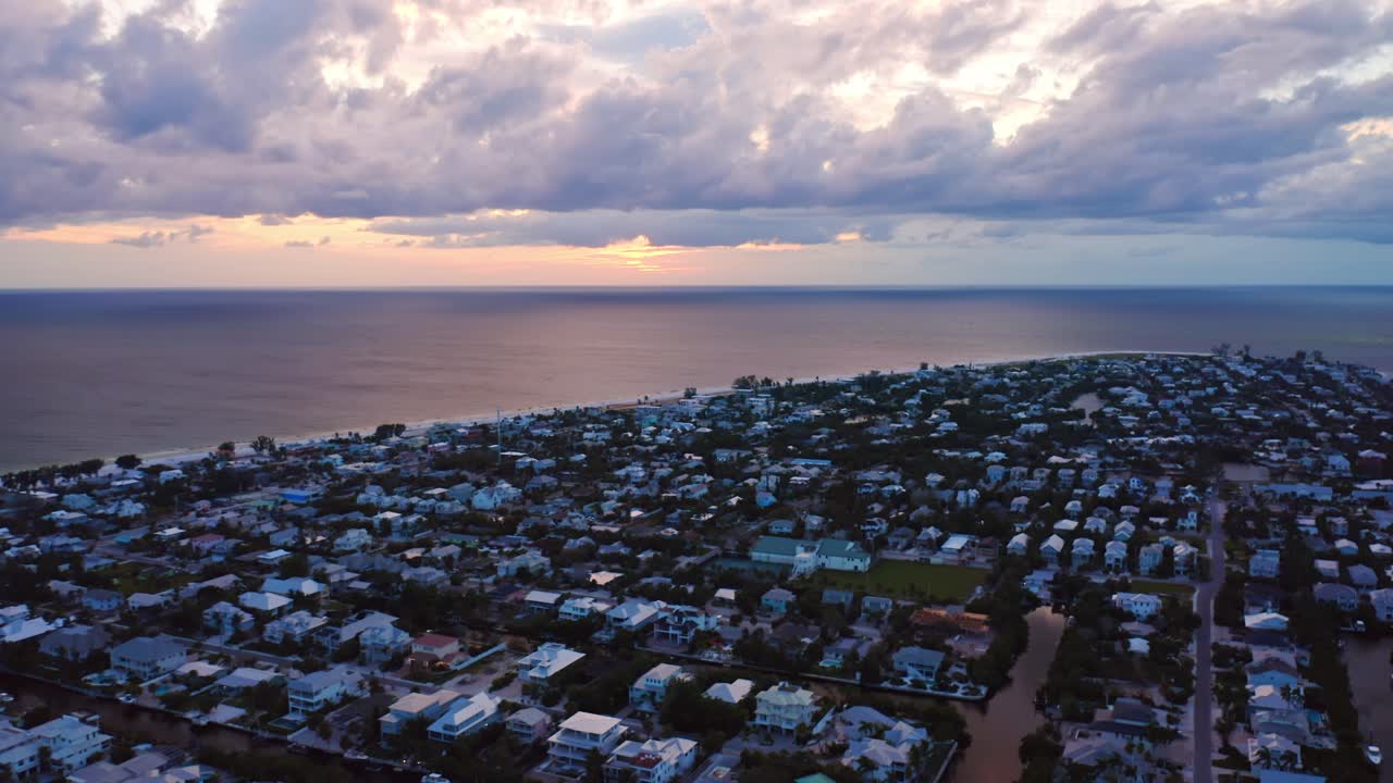 As twilight settles over Anna Maria Island, pastel homes and winding streets glow beneath streaked clouds, while the Gulf horizon fades into a golden-blue evening calm