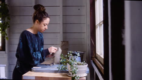 potter puts the finishing touches on clay vase in her workship