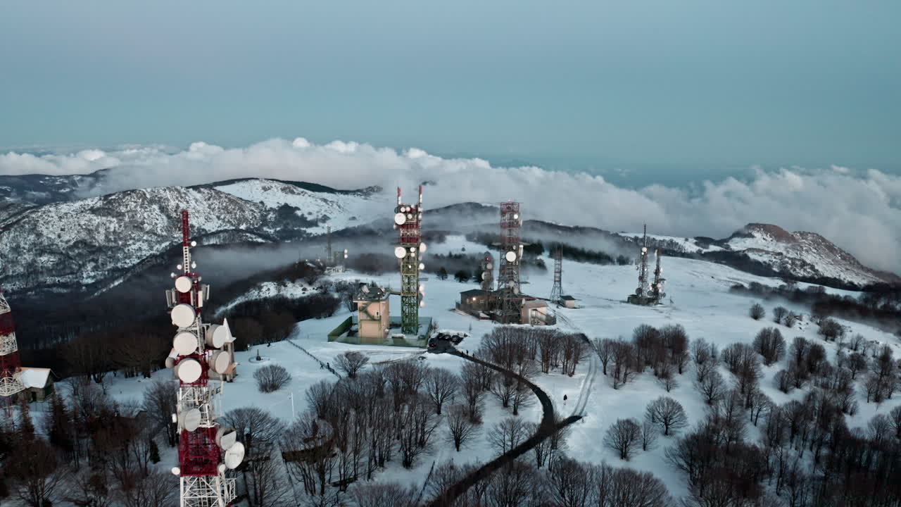 paisaje montañoso nevado con torres de radio y una iglesia, rodeado de árboles desnudos de invierno