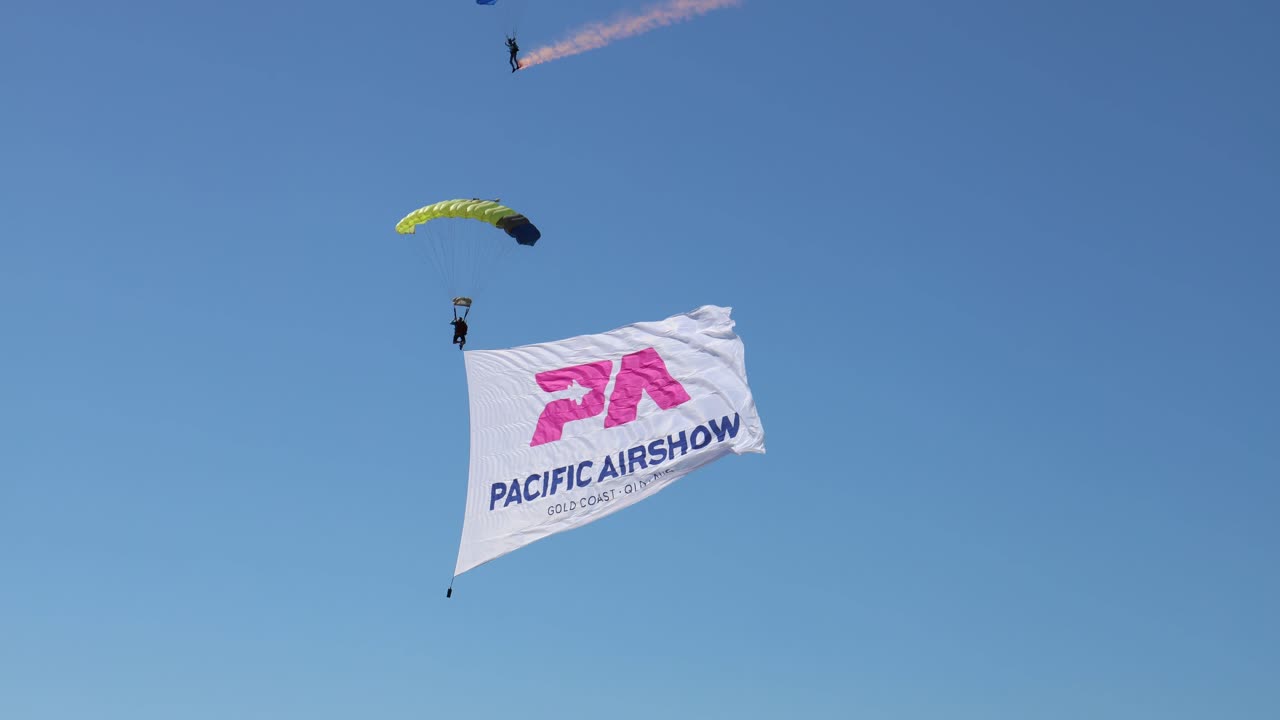 paracaidistas con pancartas descienden en un evento en la playa