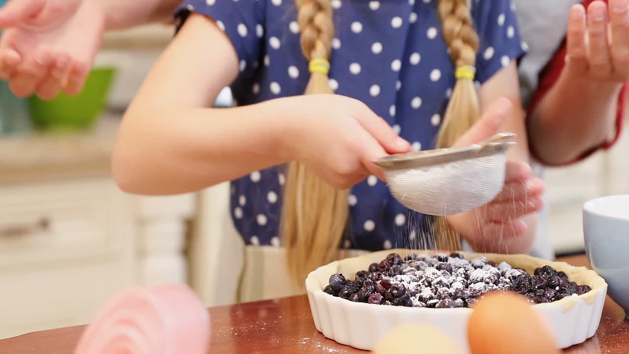 Mother and daughter sieving powder sugar on dough in the kitchen 4K 4k