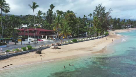 aerial view of playa punta popy, traffic on coastal road and swimming tourist in caribbean sea during cloudy day