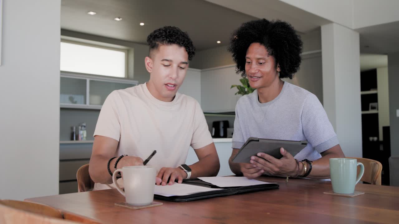 Diverse male pair reviewing folder and tablet pointing signing forms exchanging it celebrating