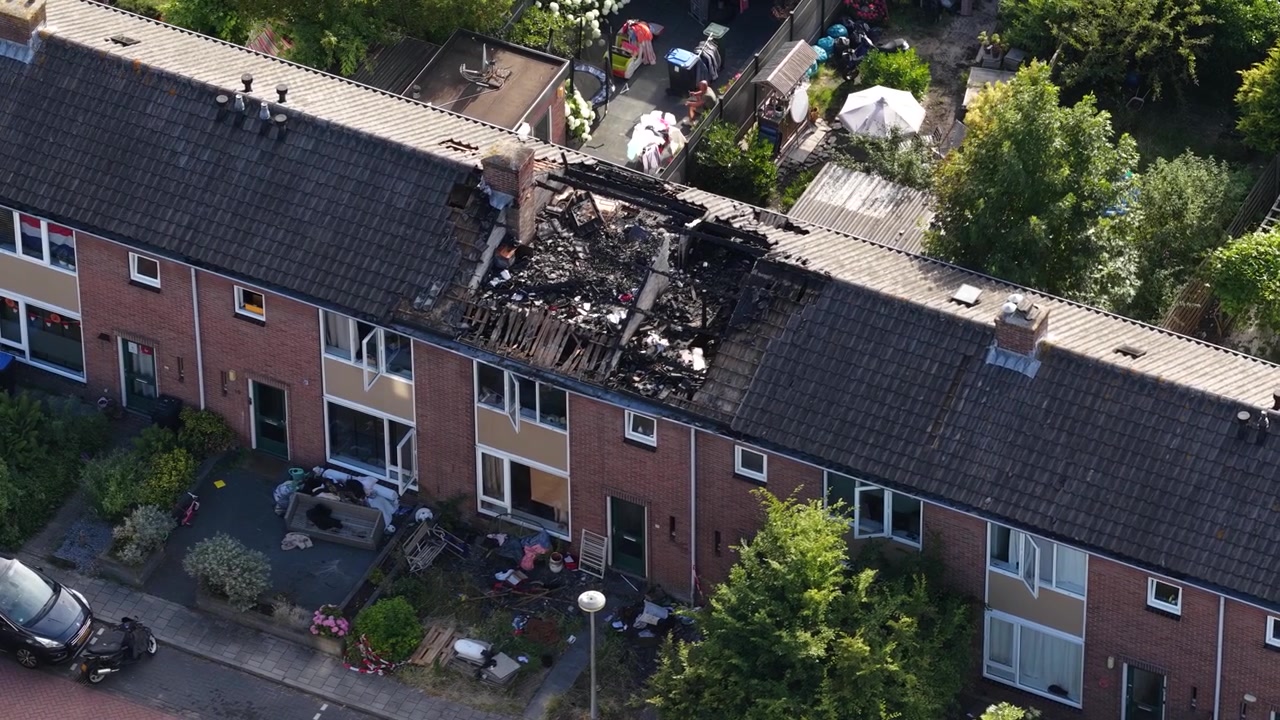 Luftperspektiv som viser de ødeleggende ettervirkningene av en husbrann i et boligområde, med den forkullede og kollapsede takkonstruksjonen som avslører bygningens interiør