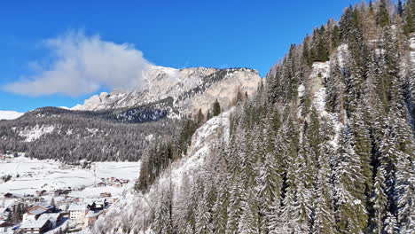 snow-covered mountain with trees and houses in selva di val gardena, italy