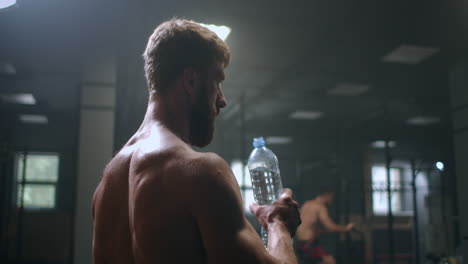 an-athletic-man-drinks-vodka-to-restore-strength-after-and-before-performing-an-exercise-in-the-gym.-drink-water-from-a-bottle-during-your-workout