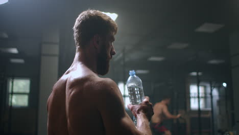 un hombre atlético bebe vodka para restaurar la fuerza después y antes de realizar un ejercicio en el gimnasio. bebe agua de una botella durante tu entrenamiento