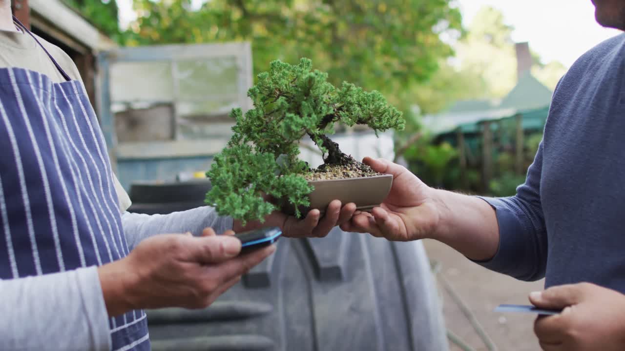 jardinero caucásico que vende plantas, usando pagos sin contacto en el centro de jardinería