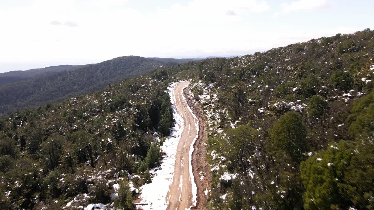 Fast push in aerial shot of dirt road in the middle of the snowy woods in Oncol Park, Chile