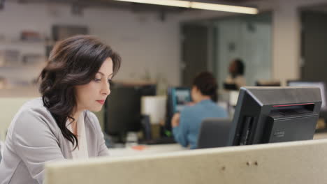 Businesswoman-executive-working-at-computer-using-device-connected-to-global-data-in-busy-corporate-office