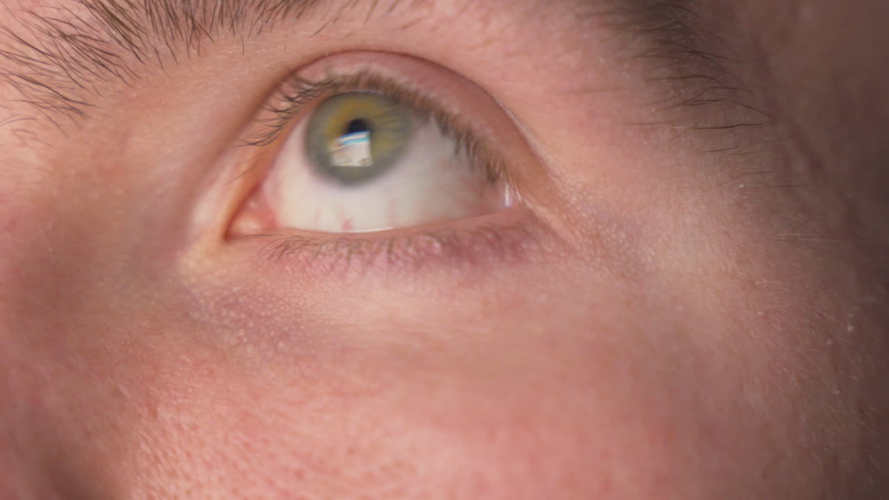 비디오 게임과 컴퓨터의 밝은 화면을 빠르게 응시하는 젊은 남자의 눈의 매크로 보기를 닫습니다.