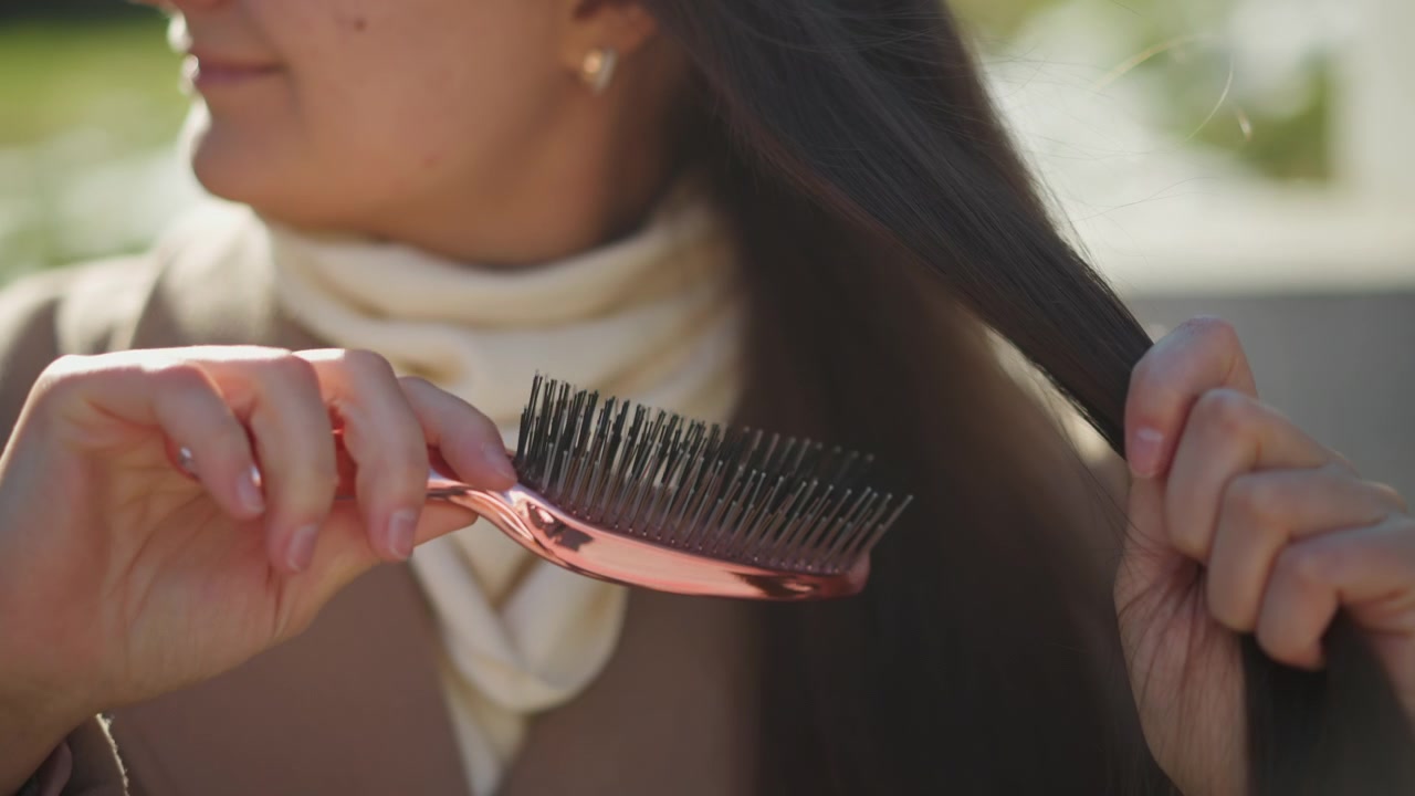 Close up of woman styling her long brown hair with hands and small pink clips in soft daylight. process involves sectioning clipping sections together to create smooth texture details