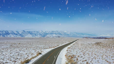 Majestätische,-Ikonische-Landstraße-Mit-Bergkette-Am-Horizont-Bei-Schneefall,-Drohnenansicht-Aus-Der-Luft