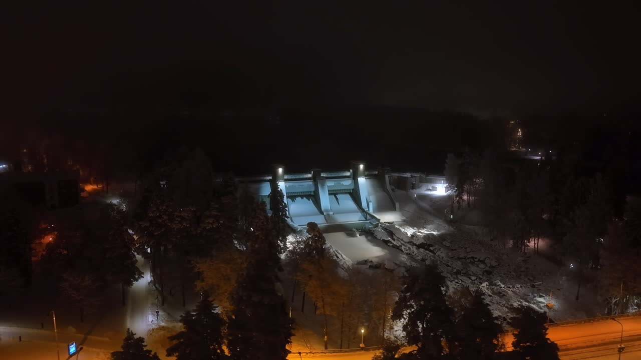 Panoramic drone shot orbiting the illuminated Imatra dam, winter night in Finland