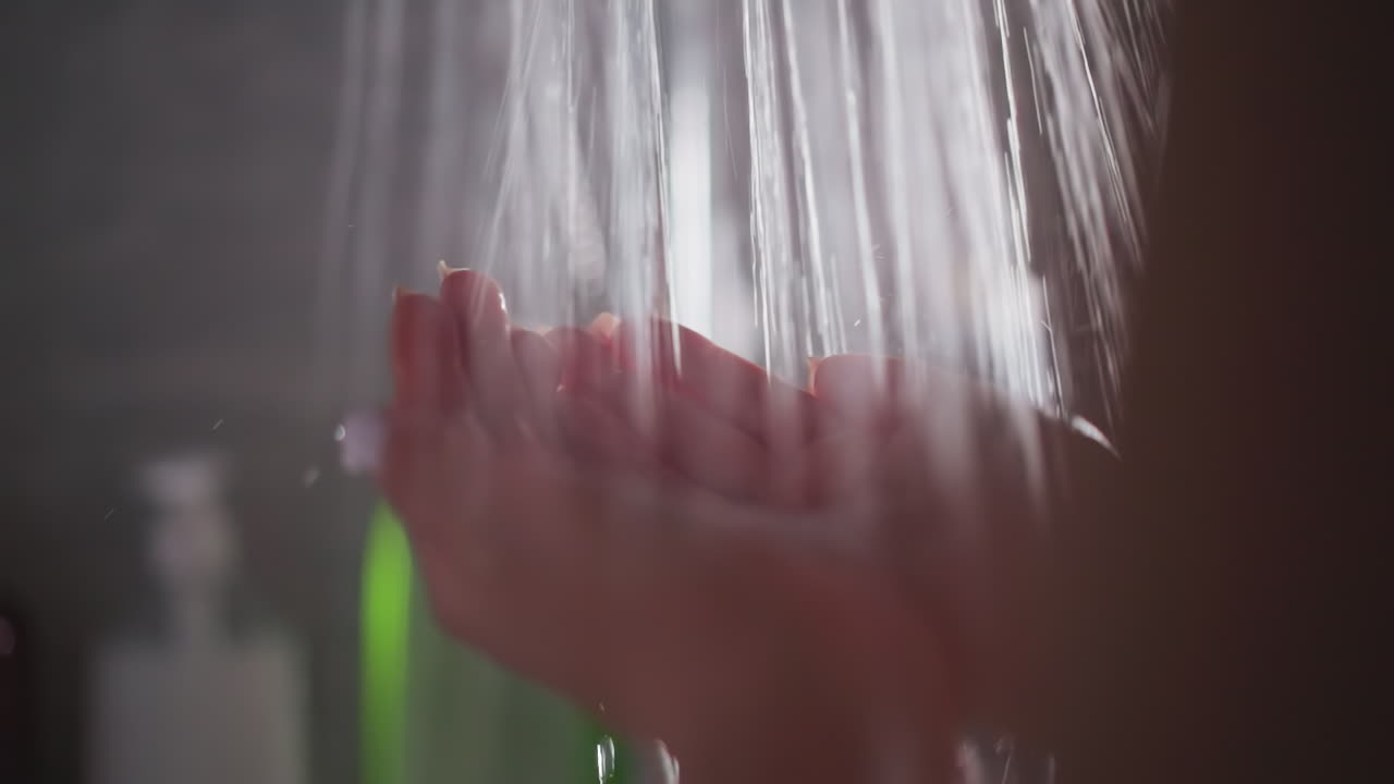 el agua cae en cascadas a través de las manos de la mujer. la mujer sostiene las manos bajo una suave corriente de agua dentro de la ducha. la dama está en la ducha bajo una corriente de agua