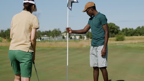 african american man and caucasian woman practicing golf on the golf course.