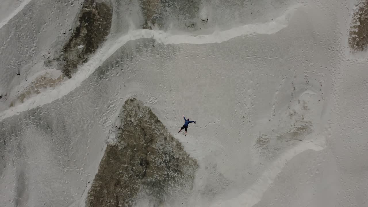 disparo de dron de alejamiento cenital de un hombre tendido en la arena y haciendo "ángeles de arena" en las dunas de arena