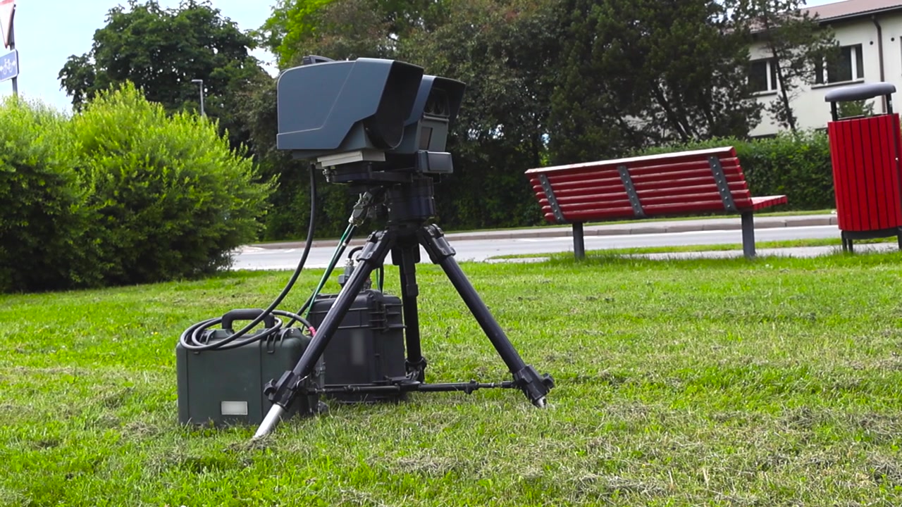Portable police speed camera on a tripod measuring traffic speed. Automated lidar system controlling vehicle velocity on a roadside to enforce speed limits and improve road safety