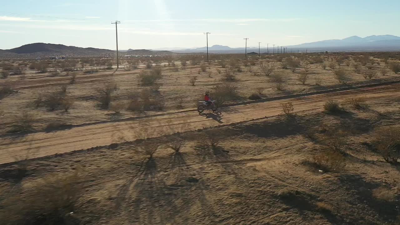 motociclista que sale de un camino de tierra hacia un sendero en una aventura todoterreno del desierto de mojave - vista aérea en cámara lenta