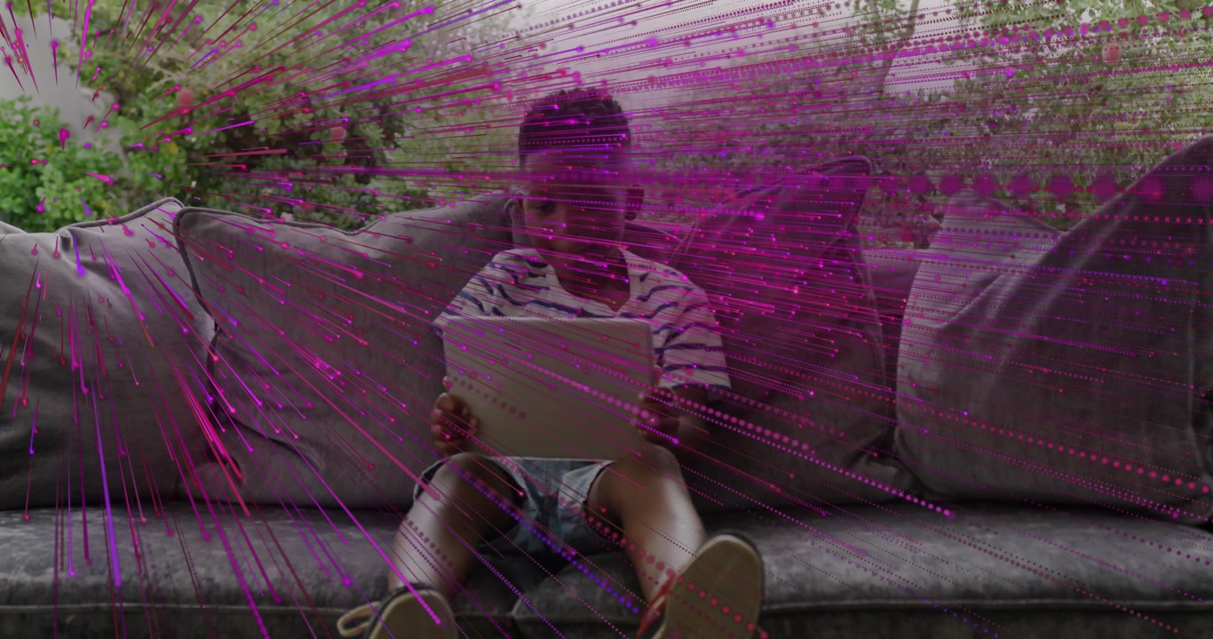 Boy tapping tablet on sofa and activating magenta streak overlay while focusing for education